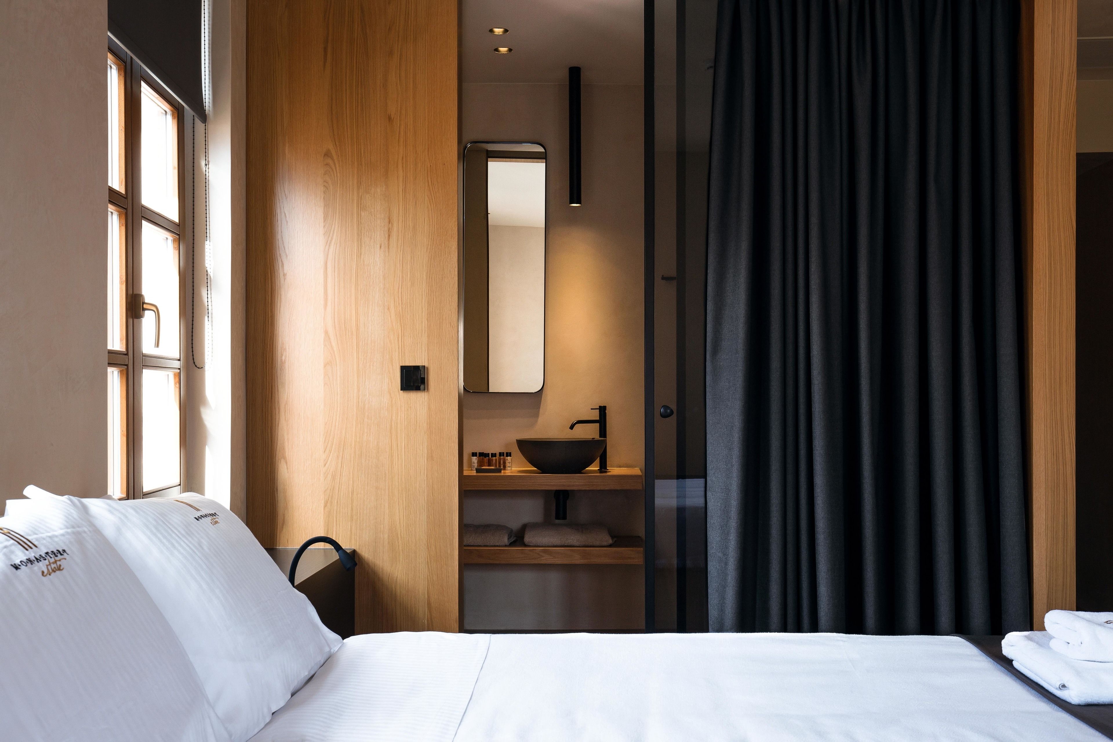 Une chambre d’hôtel comprenant un lit, une armoire en bois, une salle de bain avec un lavabo et un miroir, et une fenêtre avec des rideaux.