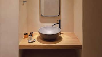 A modern bathroom with a round sink, a mirror, and a shelf with toiletries.