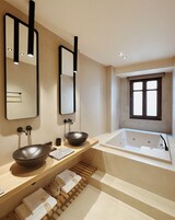 Une salle de bain moderne avec une grande baignoire, deux vasques aux formes arrondies et une fenêtre située au-dessus de la baignoire.