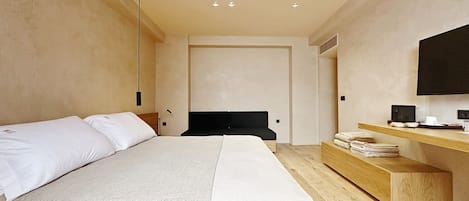 A modern hotel room with a large bed, a wooden bedside table, a flat-screen TV, and a built-in desk.