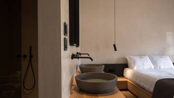 A modern bathroom with a large basin, a shower, and a bed with white bedding.