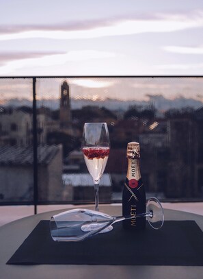 A glass of red wine and a bottle of champagne on a table with a view of a cityscape and a clock tower in the background. - Monastery Estate Venetian Harbor (Chania)