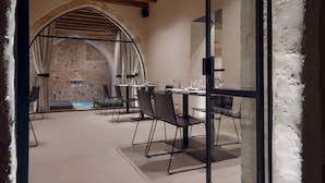 A modern dining area with a stone archway, wooden ceiling beams, and a glass partition. Tables are set with chairs and dining ware. - Monastery Estate Venetian Harbor (Chania)