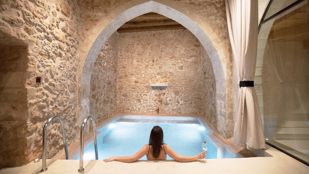 A stone-walled spa area with a large bathtub and a person relaxing in it. - Monastery Estate Venetian Harbor (Chania)