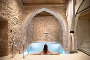A stone-walled spa area with a large bathtub and a person relaxing in it. - Monastery Estate Venetian Harbor (Chania)