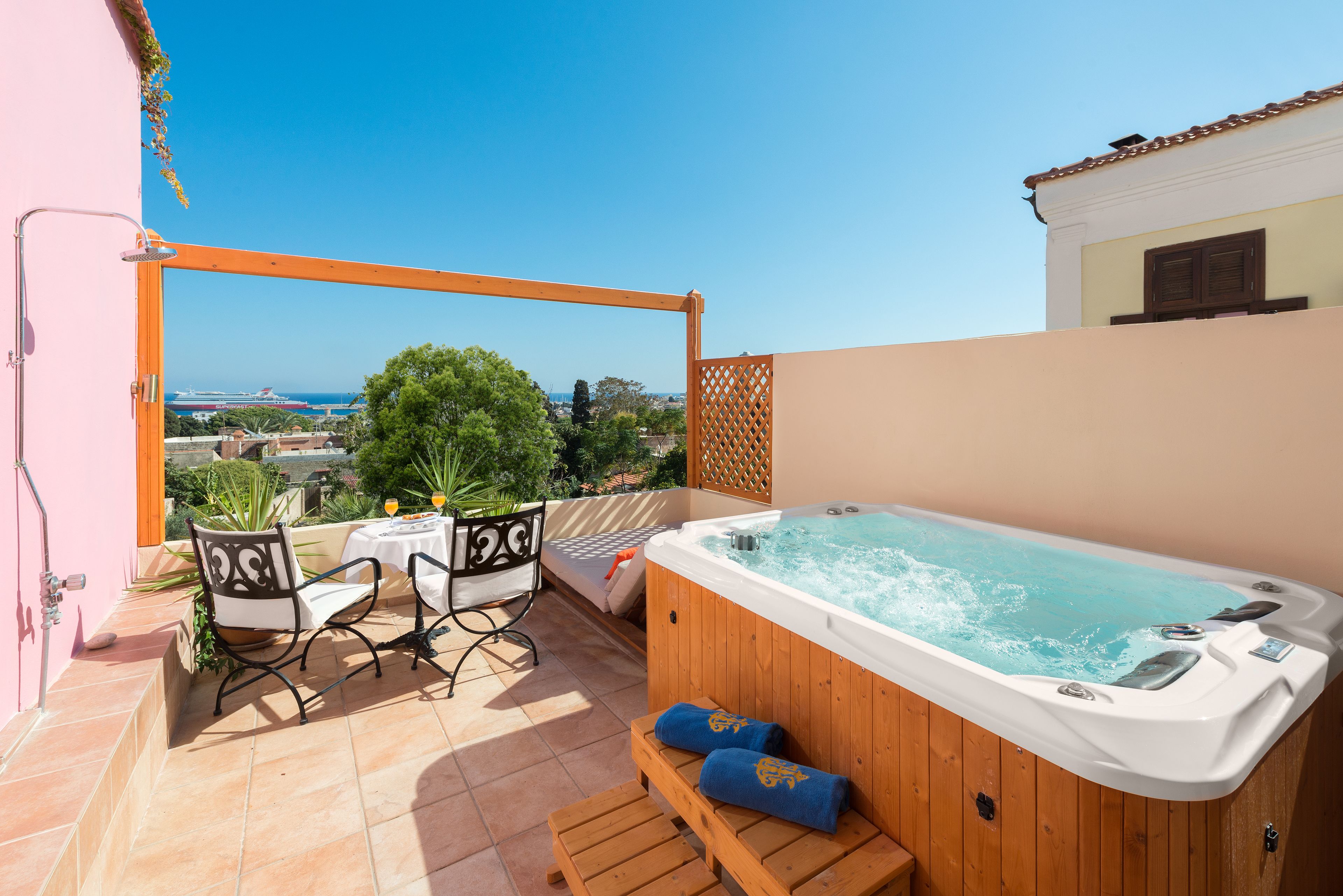Un jacuzzi en un balcón con vistas al mar, una mesa con sillas y un banco de madera.
