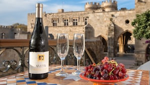 Una botella de vino Alasia Moscato D'Asti, dos copas y un bol de uvas sobre una mesa de baldosas con un castillo al fondo.