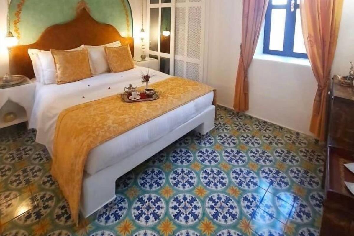 Una habitación con una cama, un ventanal con cortinas y un suelo estampado.