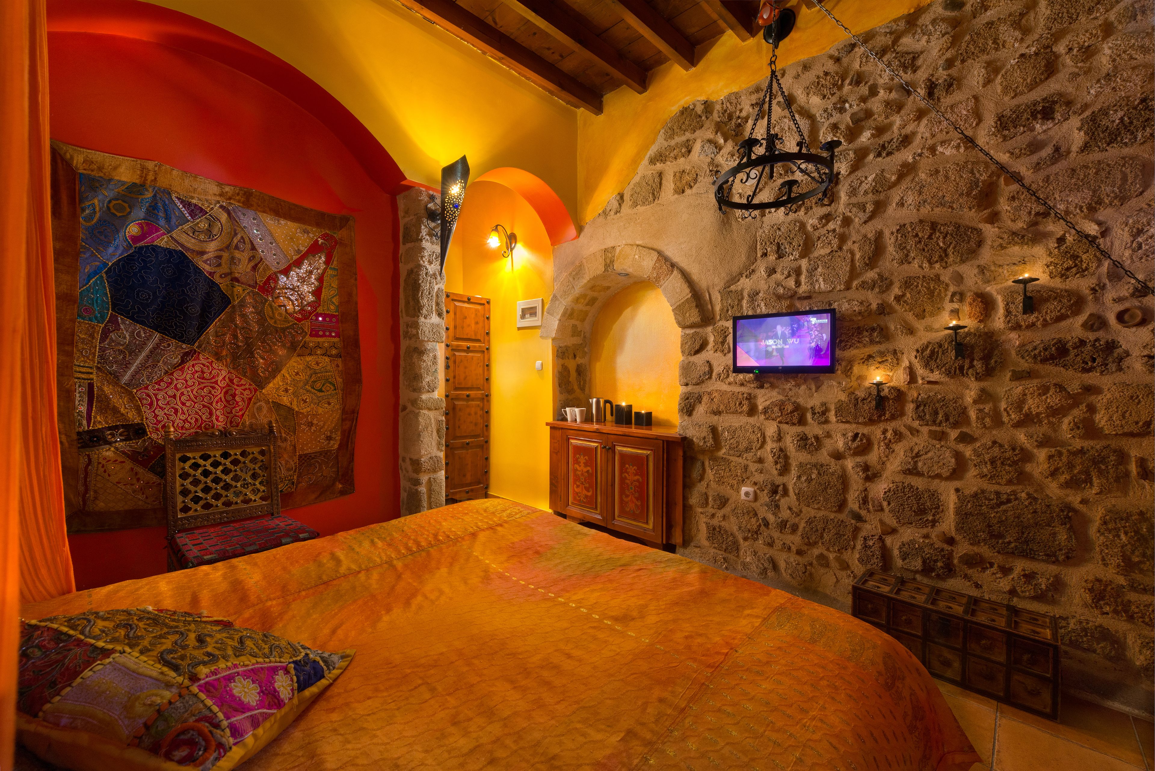 A cozy bedroom with a stone wall, a wooden bed, and a colorful tapestry.