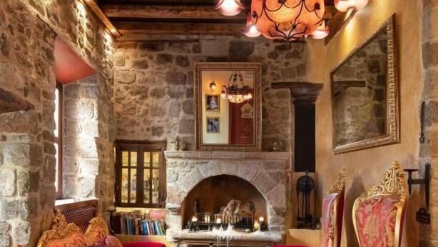 Una habitación rústica con paredes de piedra, una chimenea y sillones tapizados en rojo.