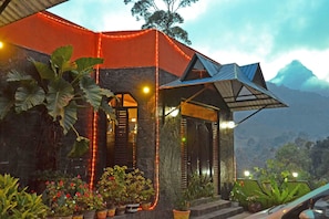 A modern house with a sloped roof, surrounded by lush greenery and potted plants. - Slightly Chilled Yellow House (Nallathanniya)