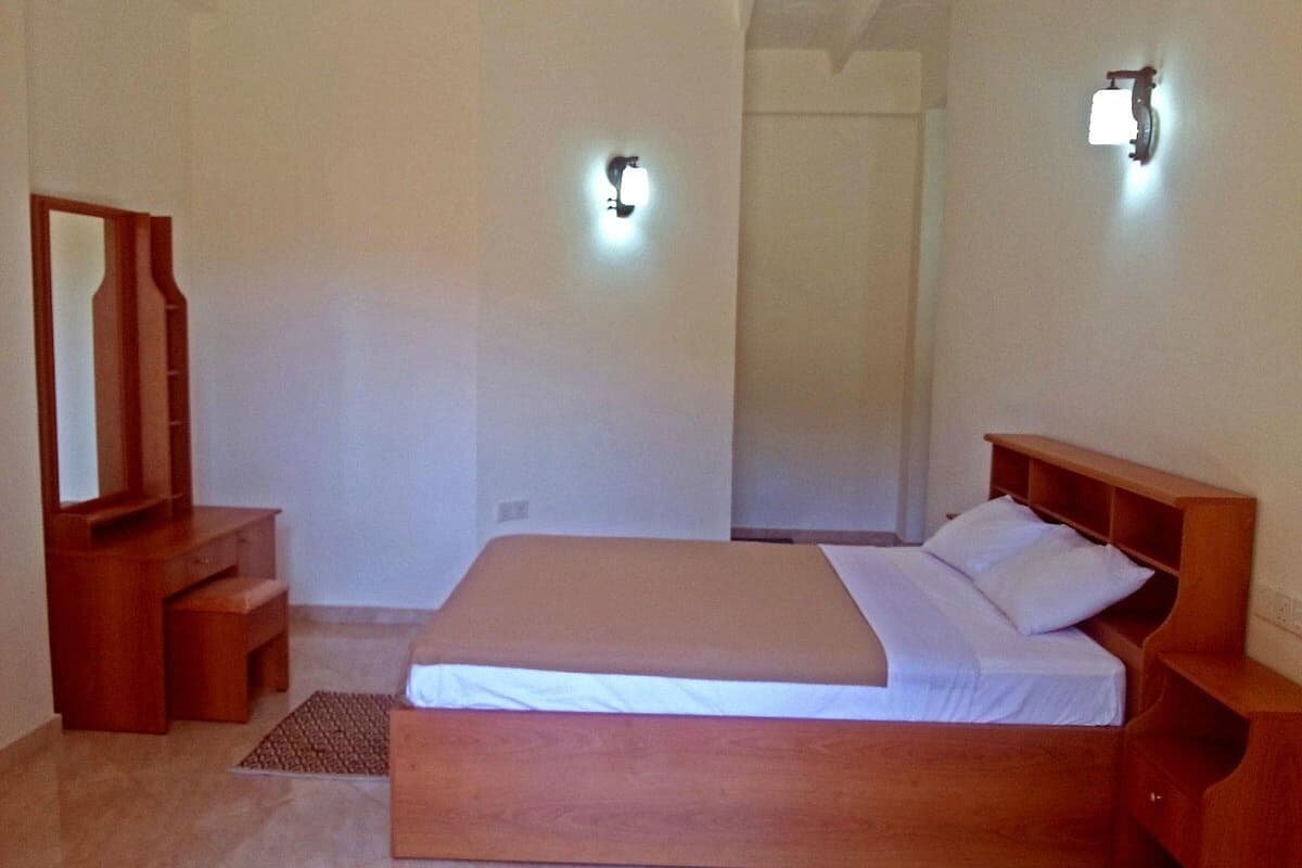 A bedroom with a wooden bed, bedside tables, a mirror, and wall-mounted lights.