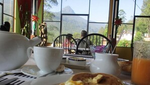 A breakfast setting with a view of mountains through large windows, a white teapot, a cup, and a plate with scrambled eggs and toast. - Slightly Chilled Yellow House (Nallathanniya)