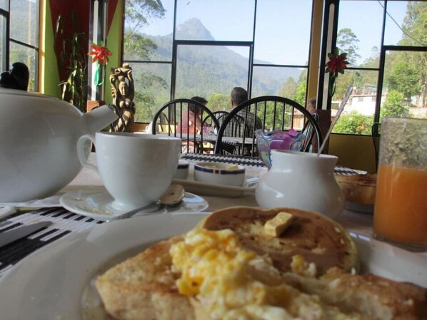 A breakfast setting with a view of mountains through large windows, a white teapot, a cup, and a plate with scrambled eggs and toast. - Slightly Chilled Yellow House (Nallathanniya)