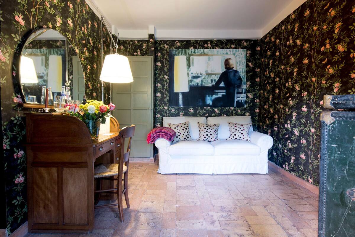 A room with floral wallpaper, a white sofa, a wooden desk with a mirror, and a lamp.