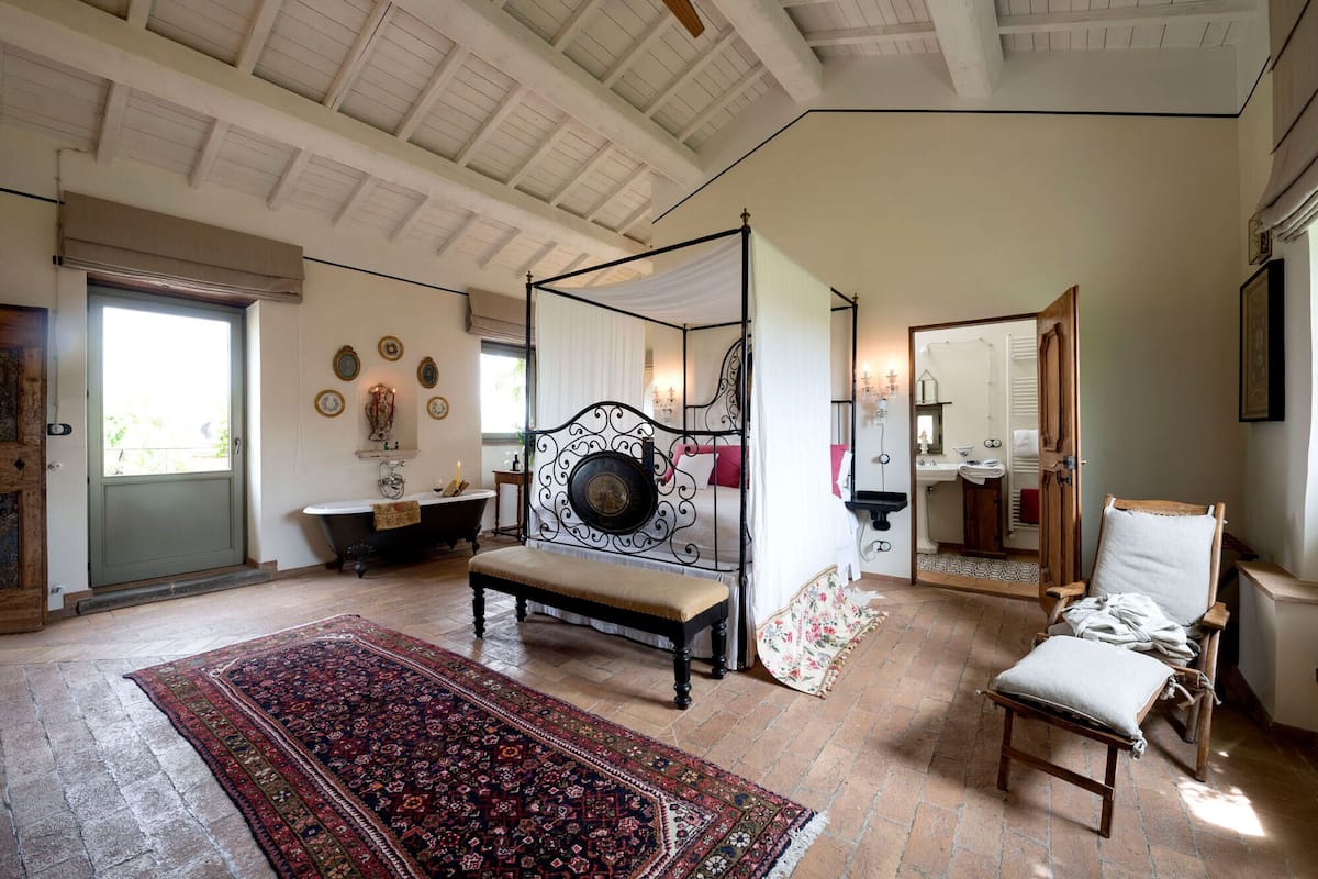 A spacious room with a large bed, a sitting area with a bench, a bathtub, and a small table.