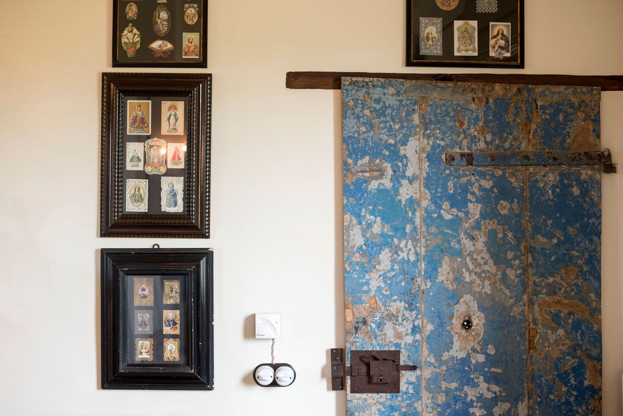A wall with multiple framed religious icons and a large, weathered door with peeling paint.