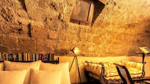 Une pièce chaleureuse avec un mur en pierre, un canapé, un fauteuil, une lampe sur pied et une bibliothèque.