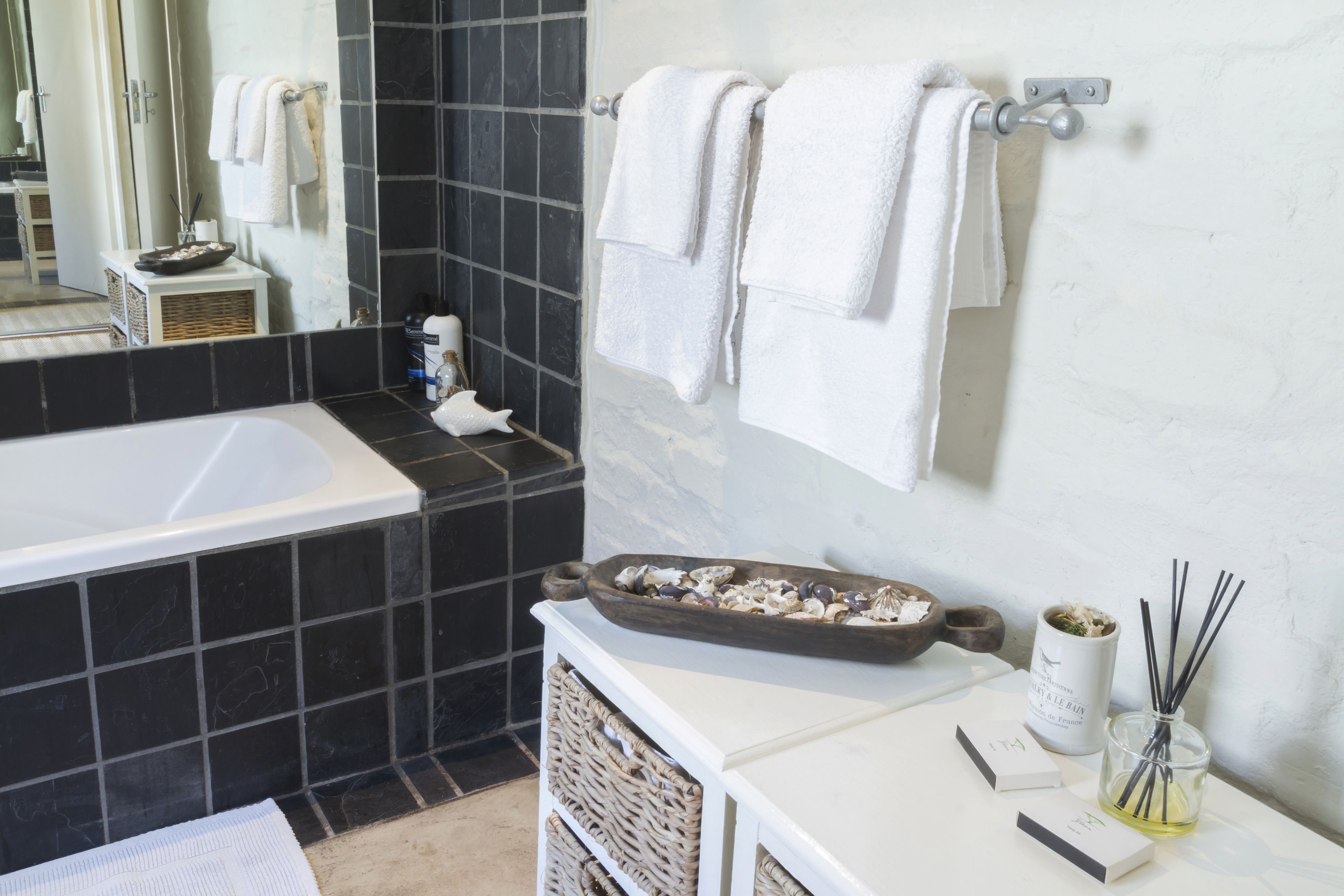 Une salle de bain équipée d’une baignoire, d’un miroir, d’un porte-serviettes, d’un lavabo et d’une petite étagère contenant des articles de toilette.
