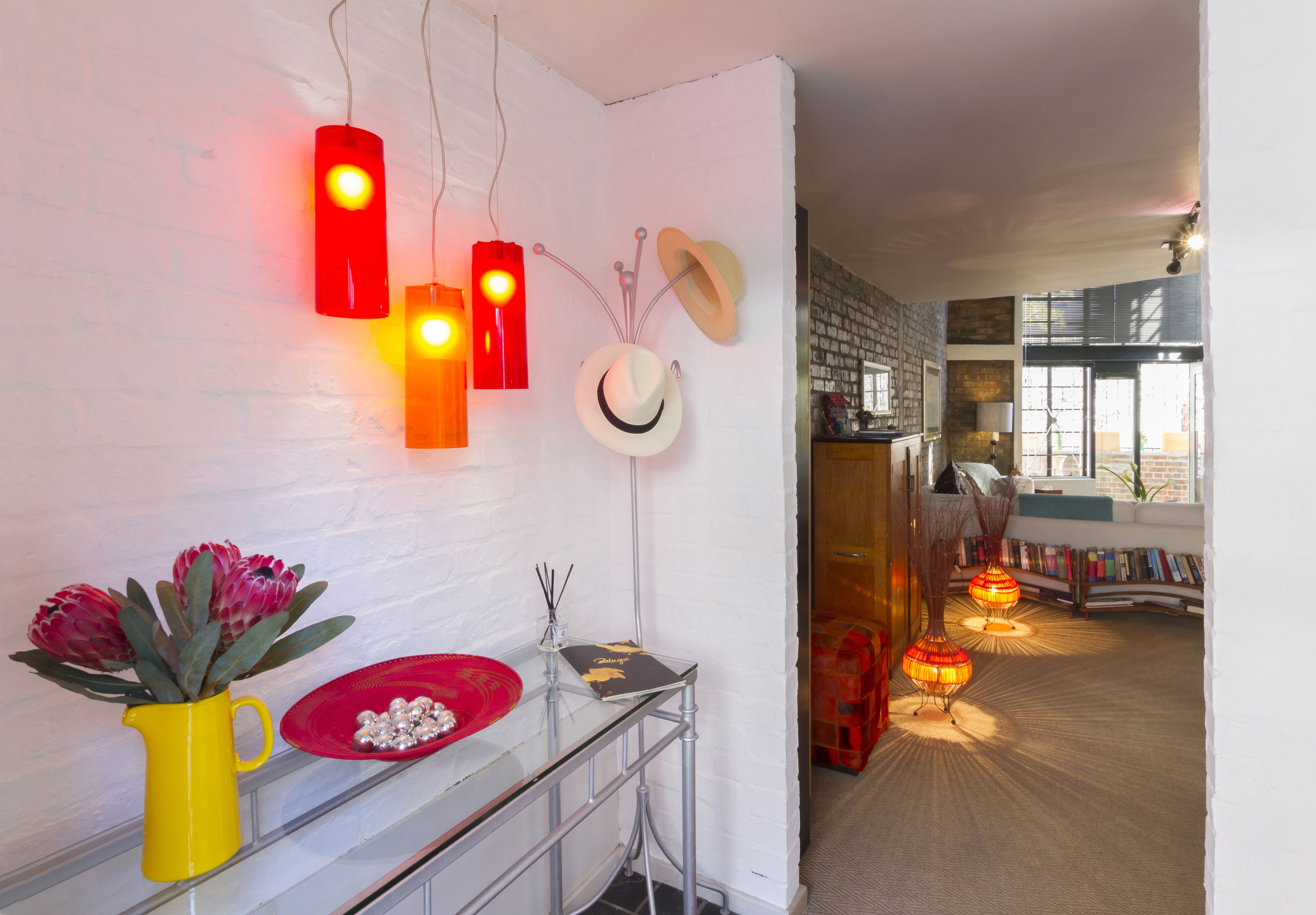 A room with a white brick wall, a glass table with a yellow vase and red bowl, and a bookshelf filled with books.