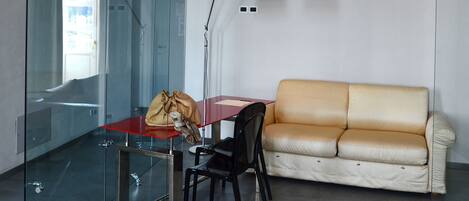 A modern room with a glass partition, a red table, a black chair, a beige sofa, and a floor lamp.