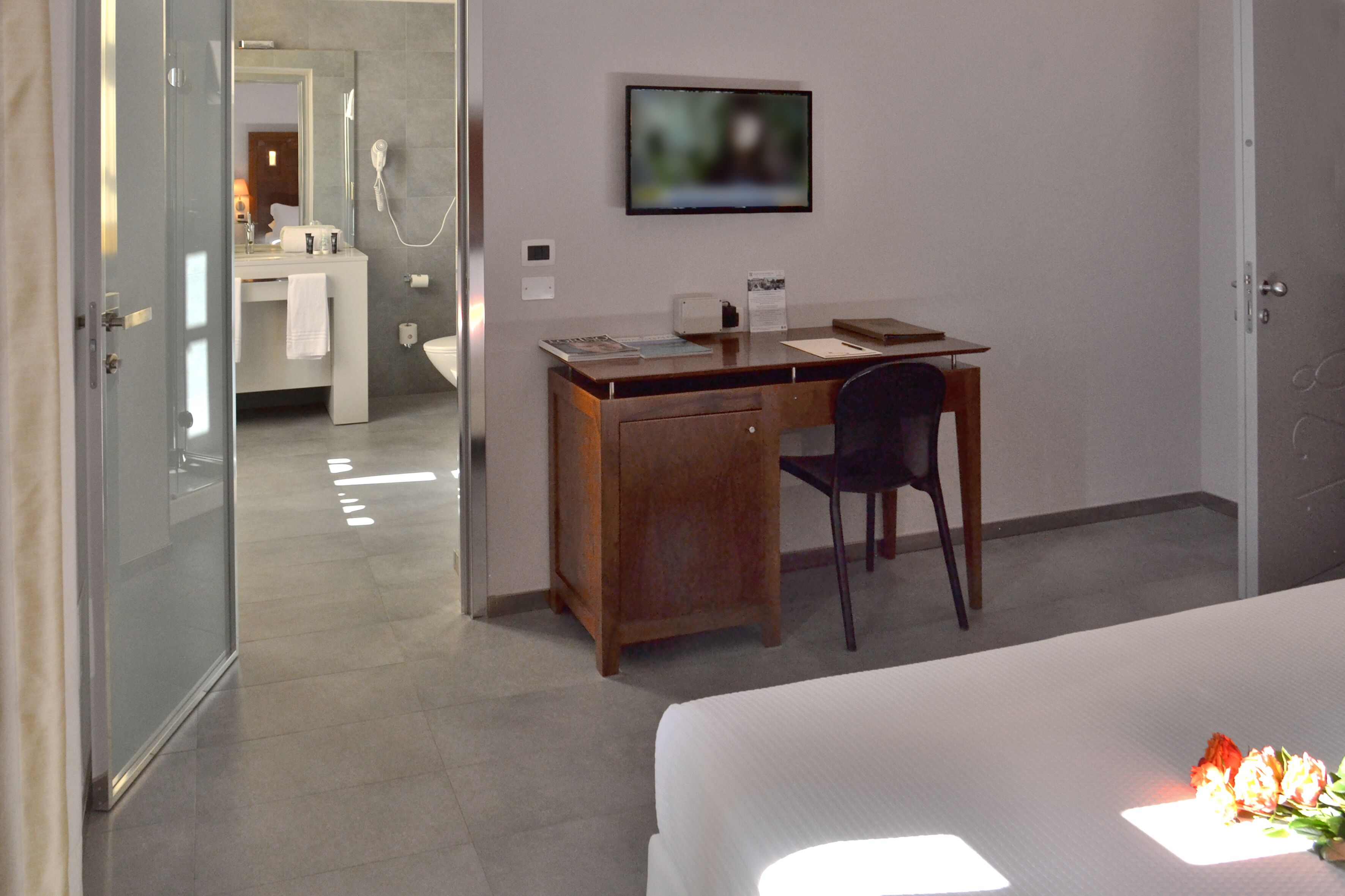 Habitación de hotel con cama, escritorio con silla, televisión y baño visible a través de una puerta abierta.