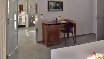 Habitación de hotel con cama, escritorio con silla, televisión y baño visible a través de una puerta abierta.
