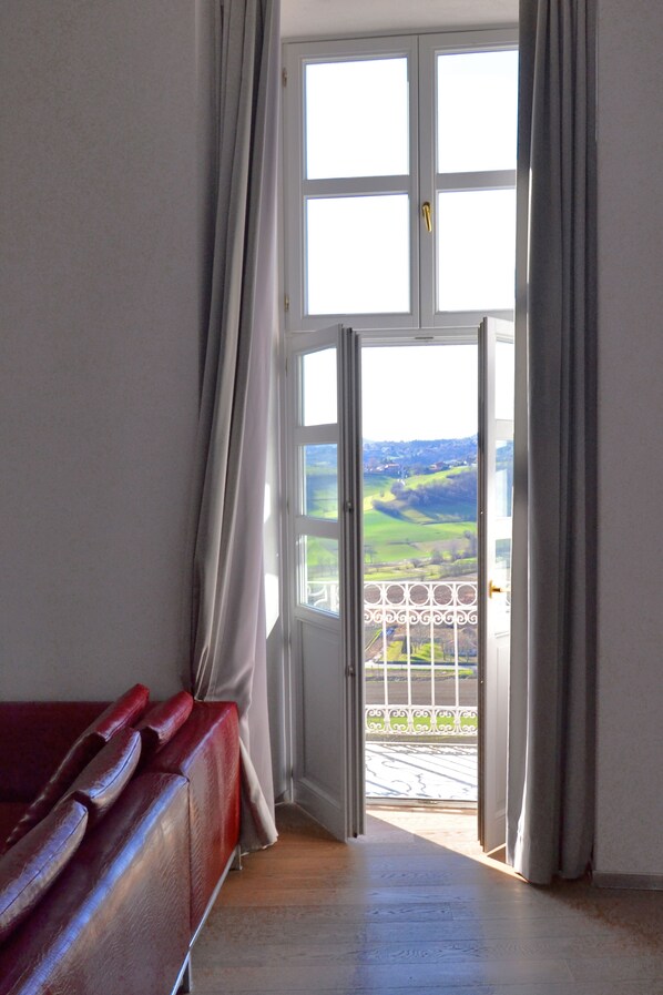 Una habitación con un sofá rojo, suelo de madera y un amplio ventanal con cortinas.