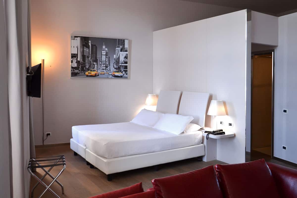 Een hotelkamer met een bed, twee bedlampen, een tv aan de muur en een schilderij van een stadsgezicht.