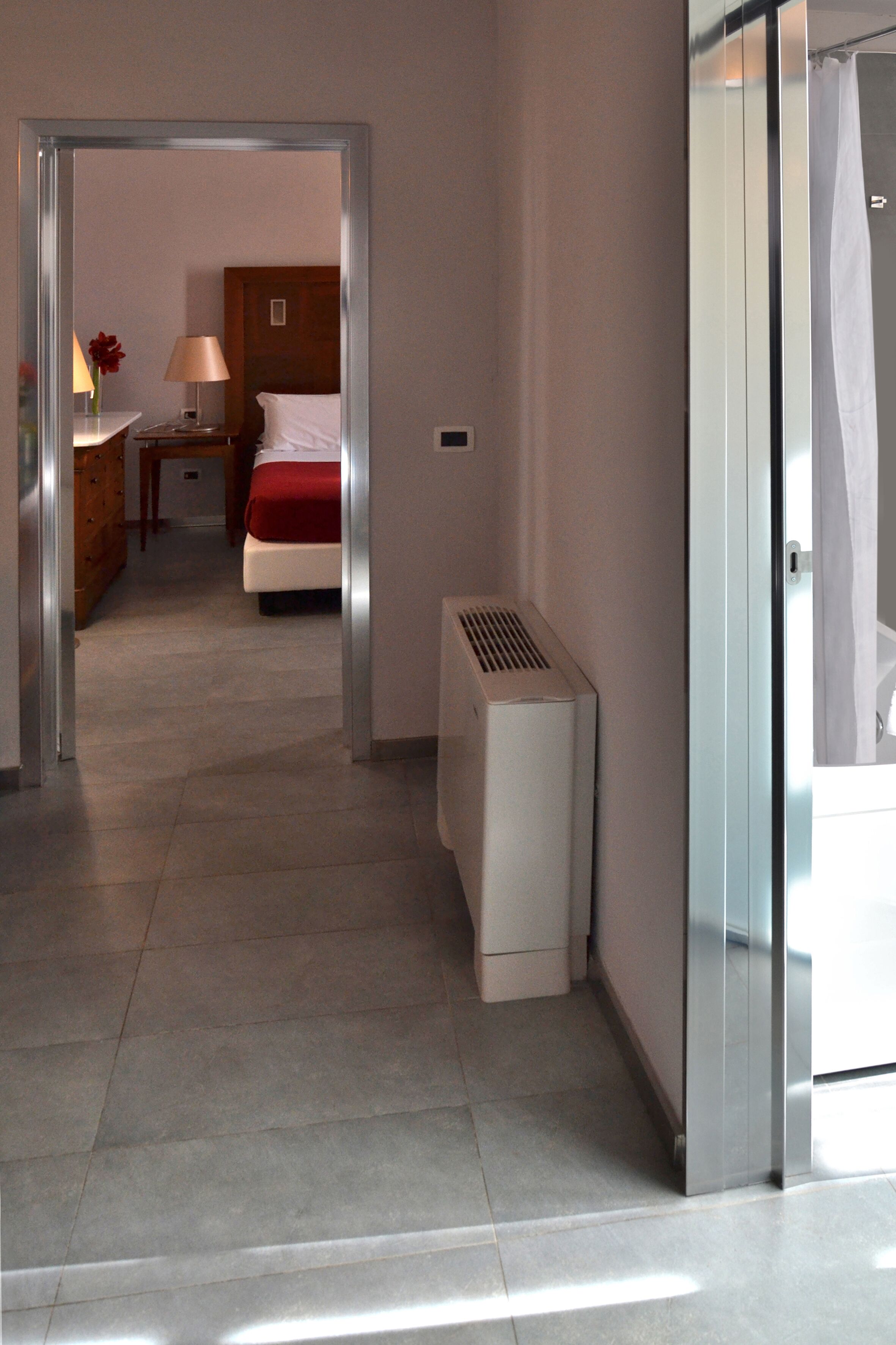 Un corridoio d'albergo con un letto, un comodino, una lampada e un termosifone.