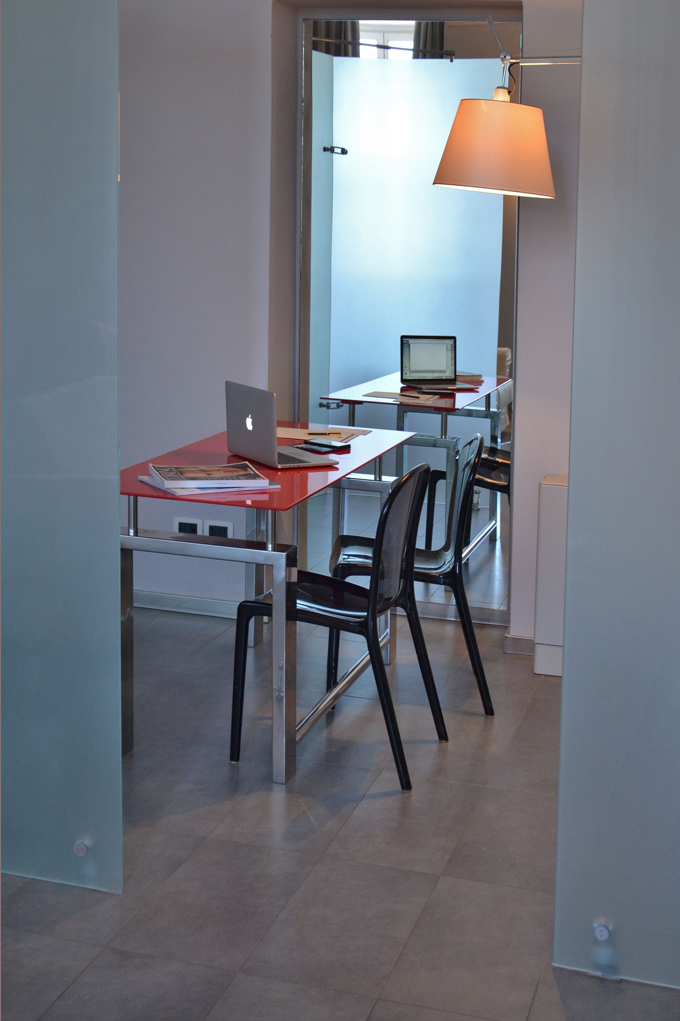 A modern office space with a red desk, a laptop, a chair, and a hanging lamp.