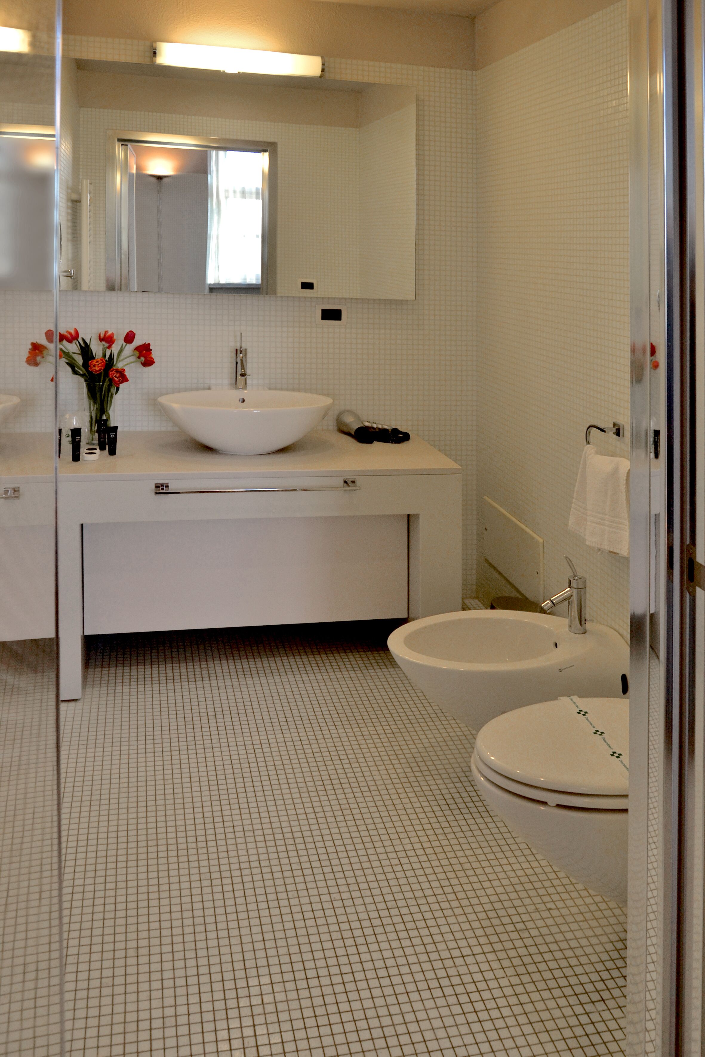 Une salle de bain avec un lavabo blanc, un miroir et deux toilettes.