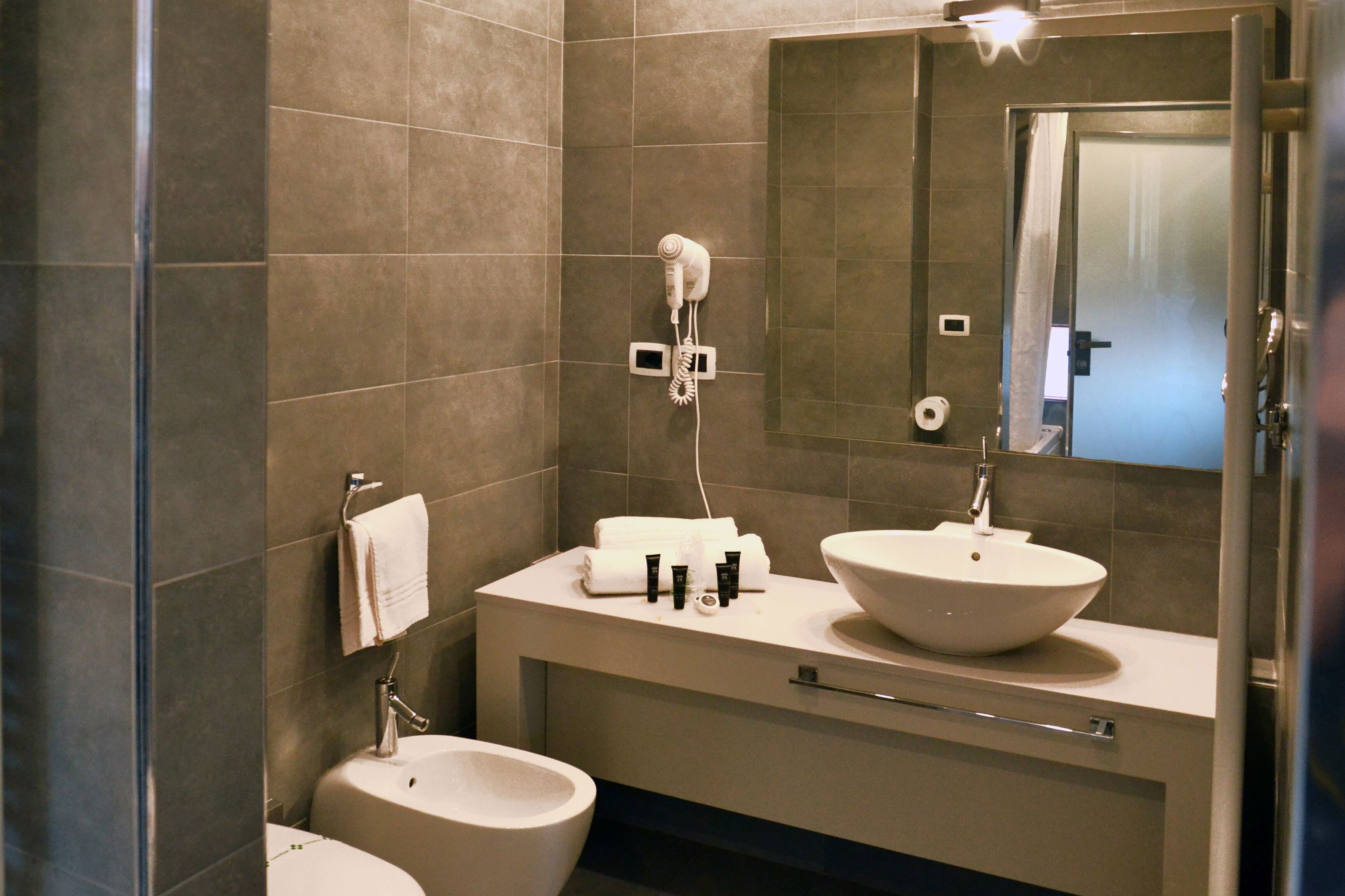 A modern bathroom with a large sink, a toilet, and a hairdryer mounted on the wall.