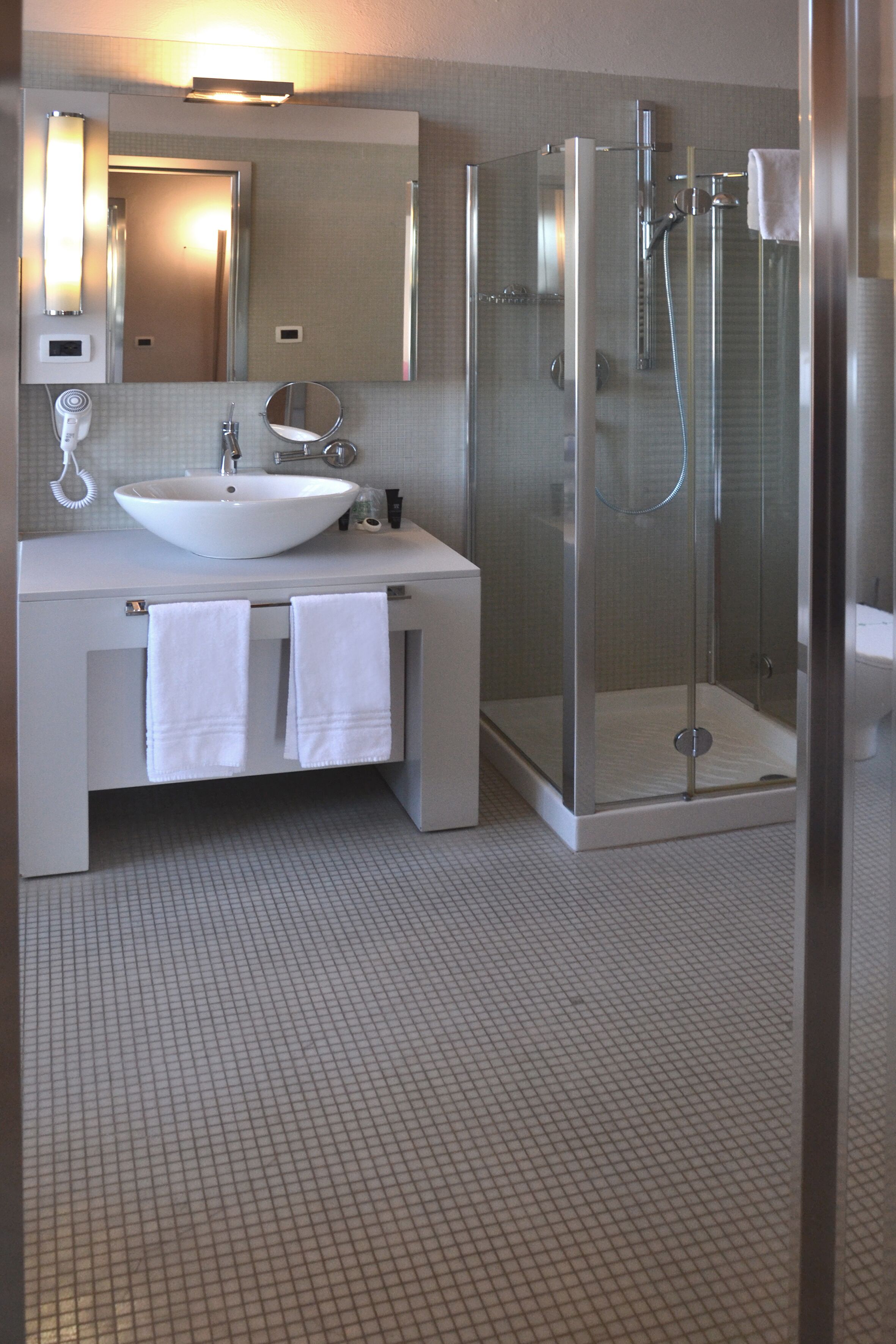 A modern bathroom with a large mirror, a white sink, and a glass-enclosed shower.