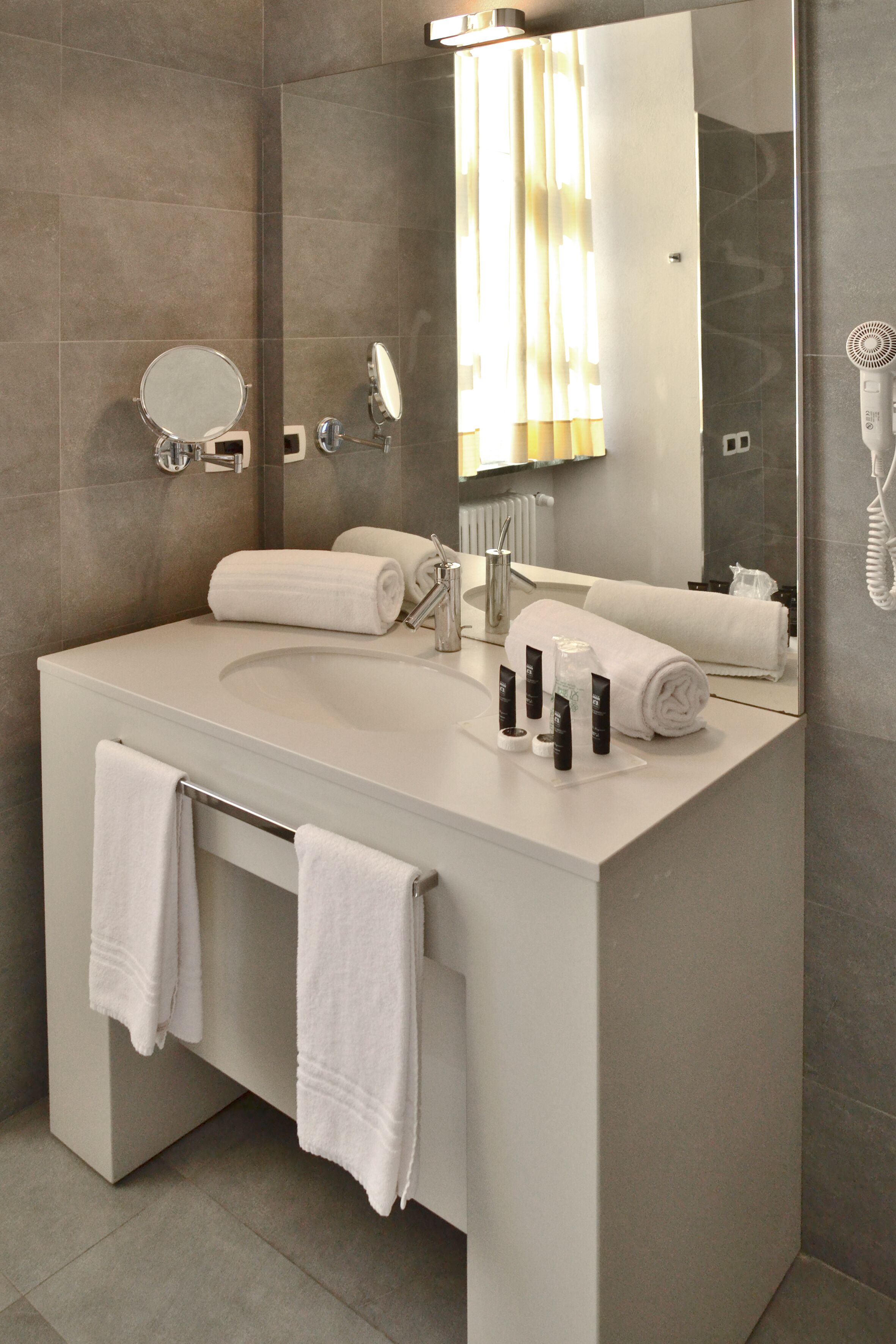 A modern bathroom with a large sink, two mirrors, a towel rack, and a hairdryer.