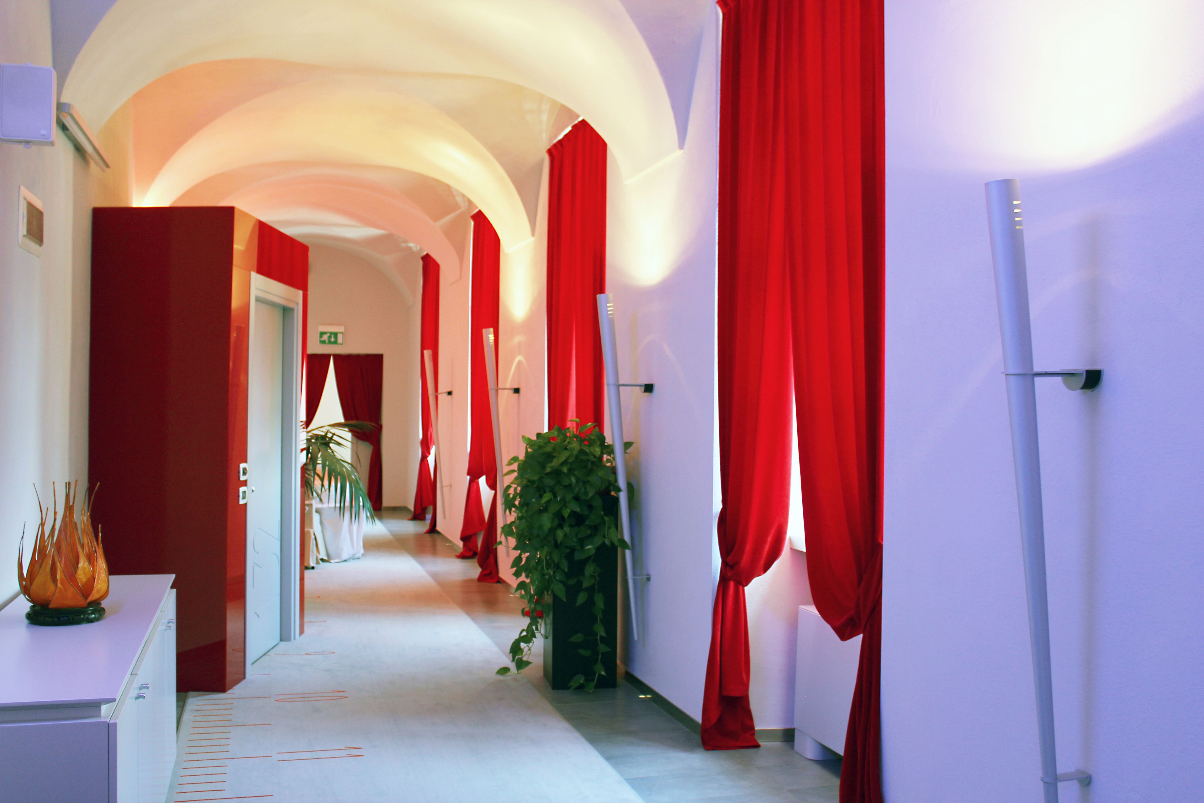 A hotel corridor with red curtains, a potted plant, and a white reception desk.