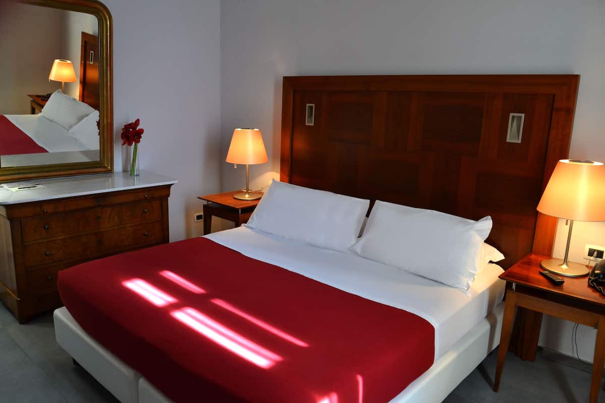Een hotelkamer met een groot bed, een houten hoofdbord, twee nachtkastjes met lampen, een dressoir en een spiegel.