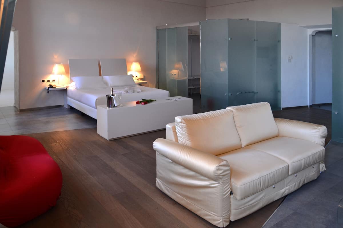 Een moderne hotelkamer met een bed, een bank, een rode stoel en een glazen kast.