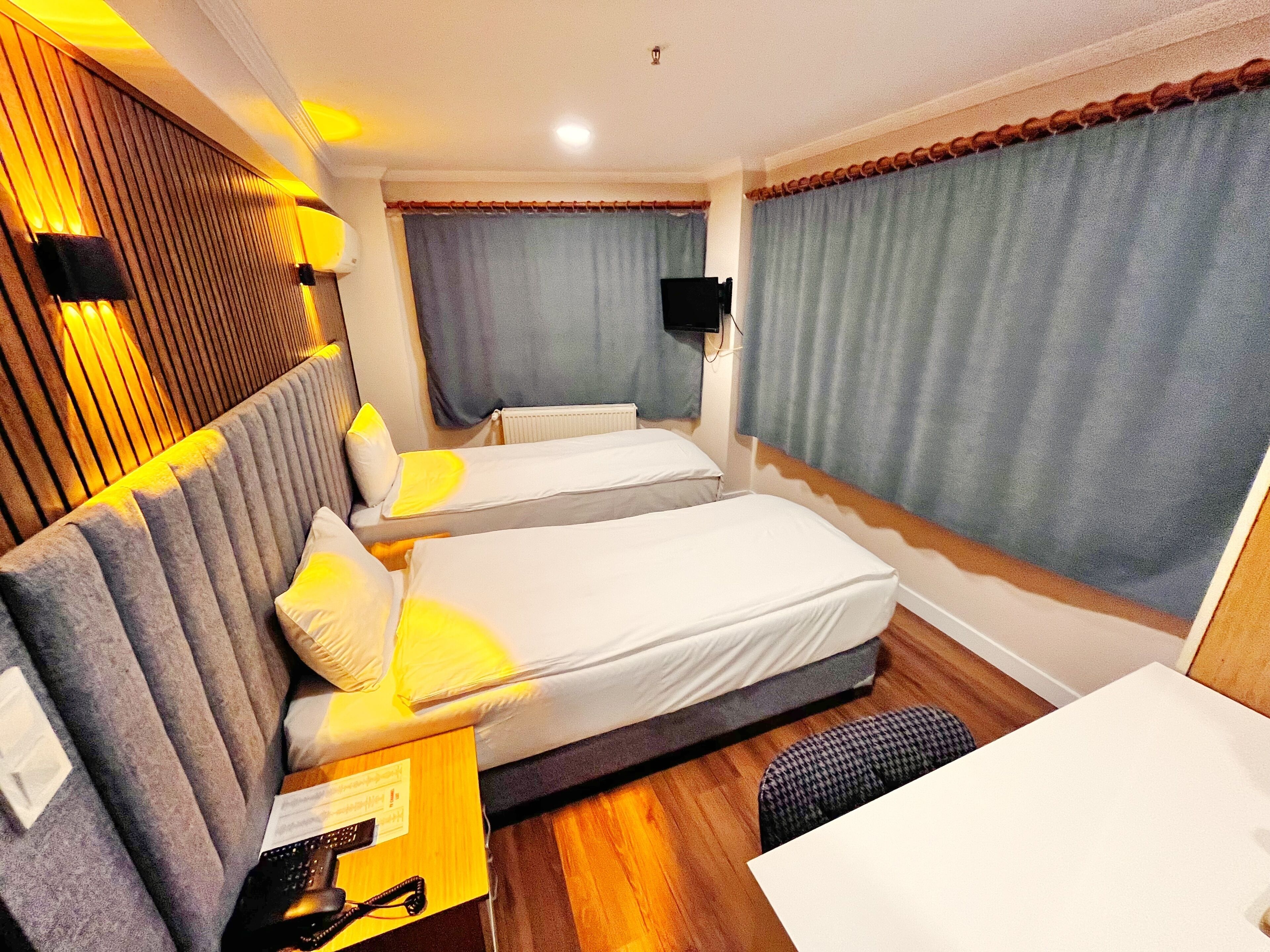 A hotel room with two beds, a desk, a chair, a TV, and a window with curtains.