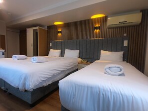 Une chambre d’hôtel avec deux lits, une tête de lit en bois, un téléphone sur la table de chevet et un climatiseur fixé au mur.