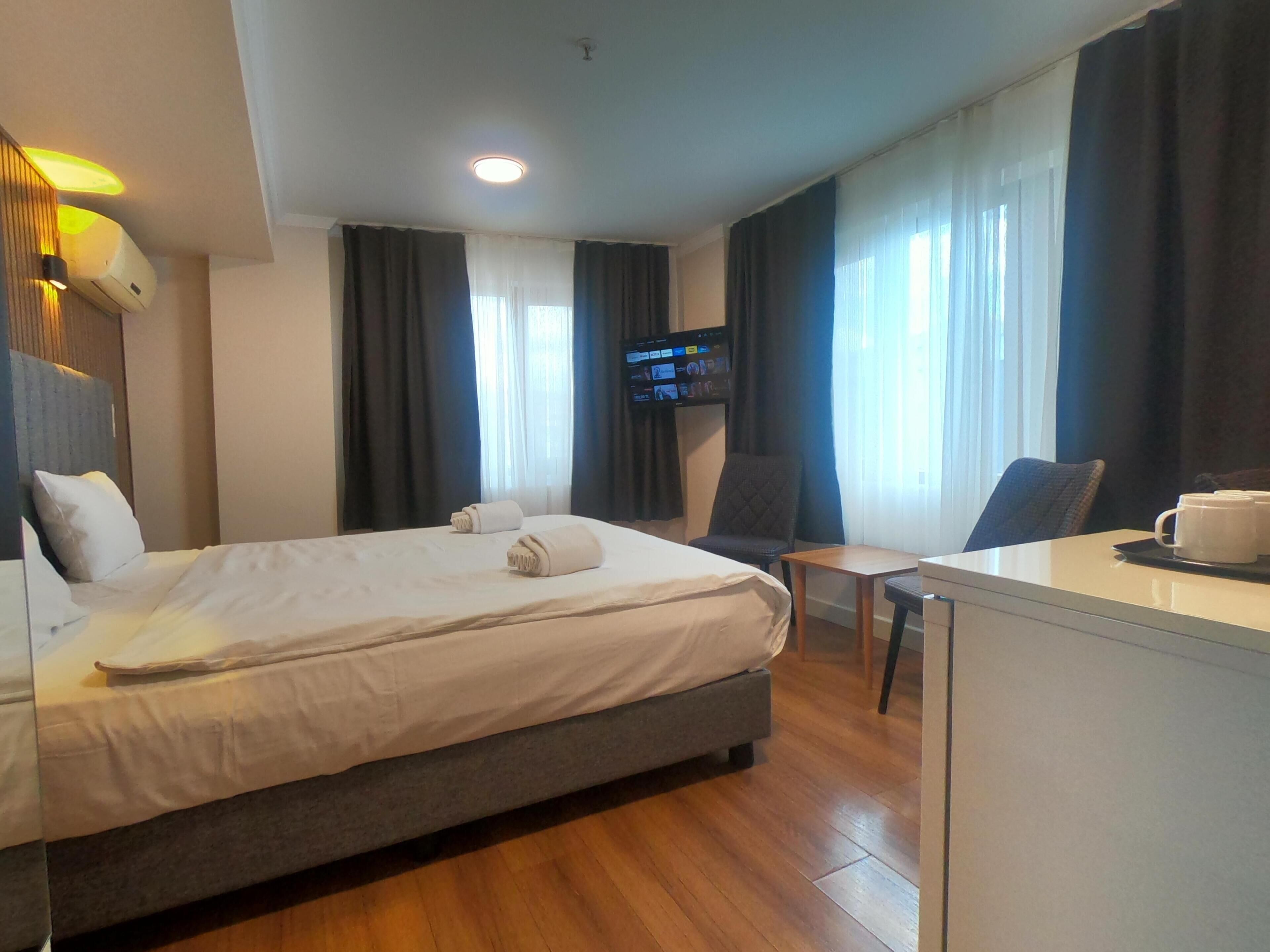 A hotel room with a bed, a desk, a chair, a television, and a window with curtains.
