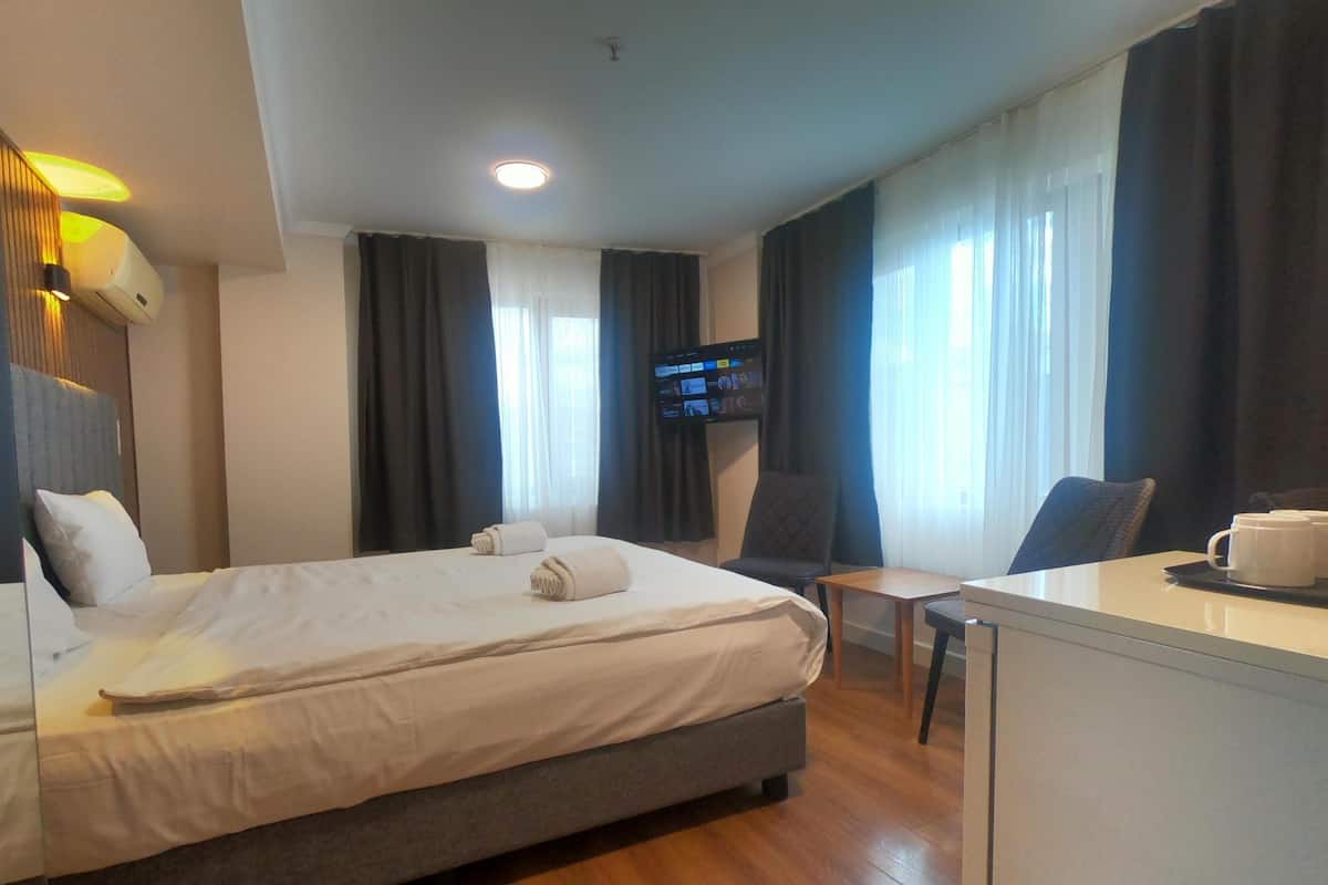 A hotel room with a bed, a desk, a chair, a television, and a window with curtains.