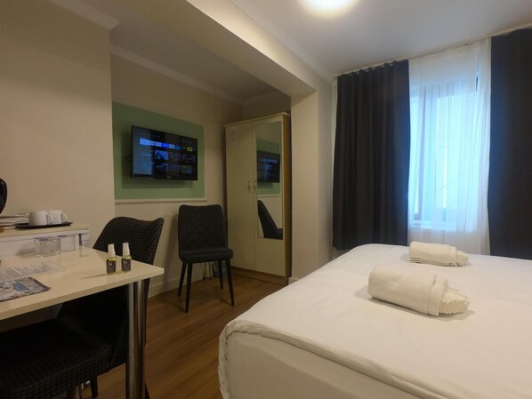 Une chambre d’hôtel avec un lit, un bureau et une chaise, un téléviseur fixé au mur et une fenêtre avec des rideaux.