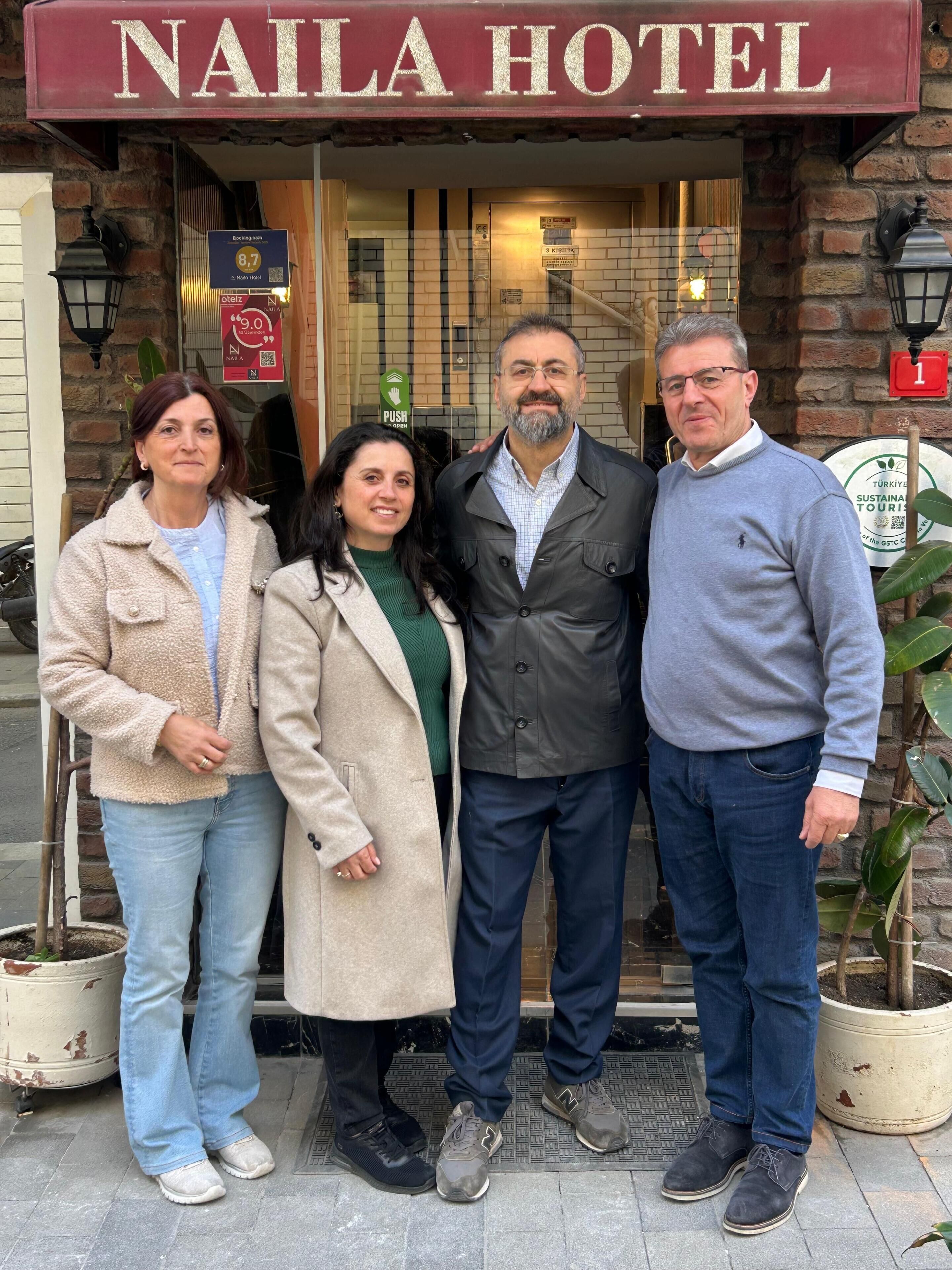 Un groupe de personnes se tient devant l’entrée d’un hôtel, et une enseigne indique « HÔTEL NAILA ».