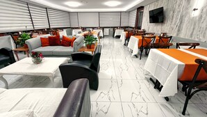 A modern restaurant with a marble floor, white and orange tablecloths, and a flat-screen TV on the wall. - Naila Hotel (Istanbul)