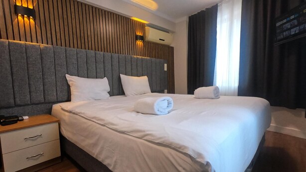 A hotel room with a large bed, a nightstand, a wall-mounted light, and a flat-screen TV. - Naila Hotel (Istanbul)