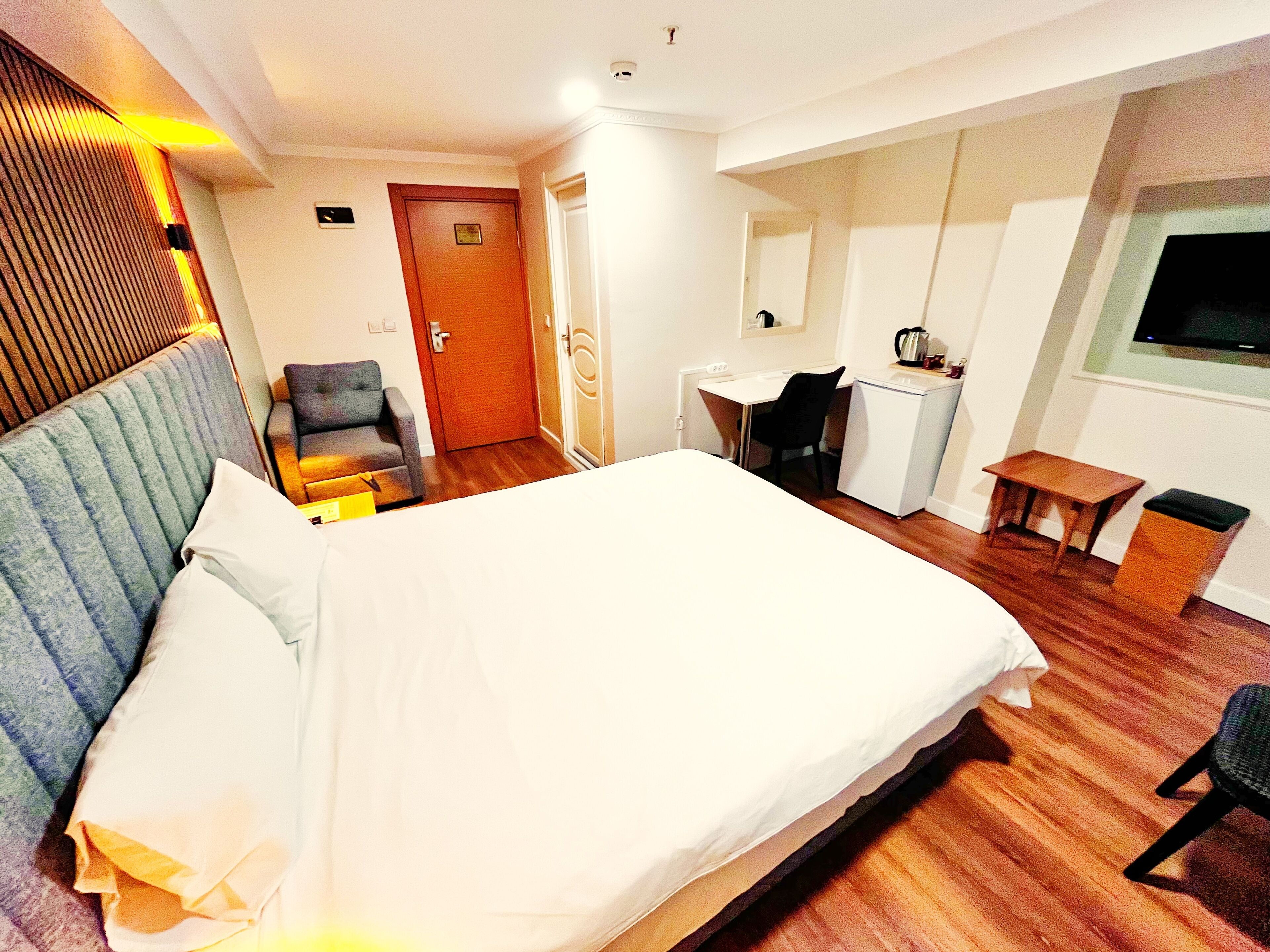 A hotel room with a bed, a desk, a chair, a small table, a TV, and a door.
