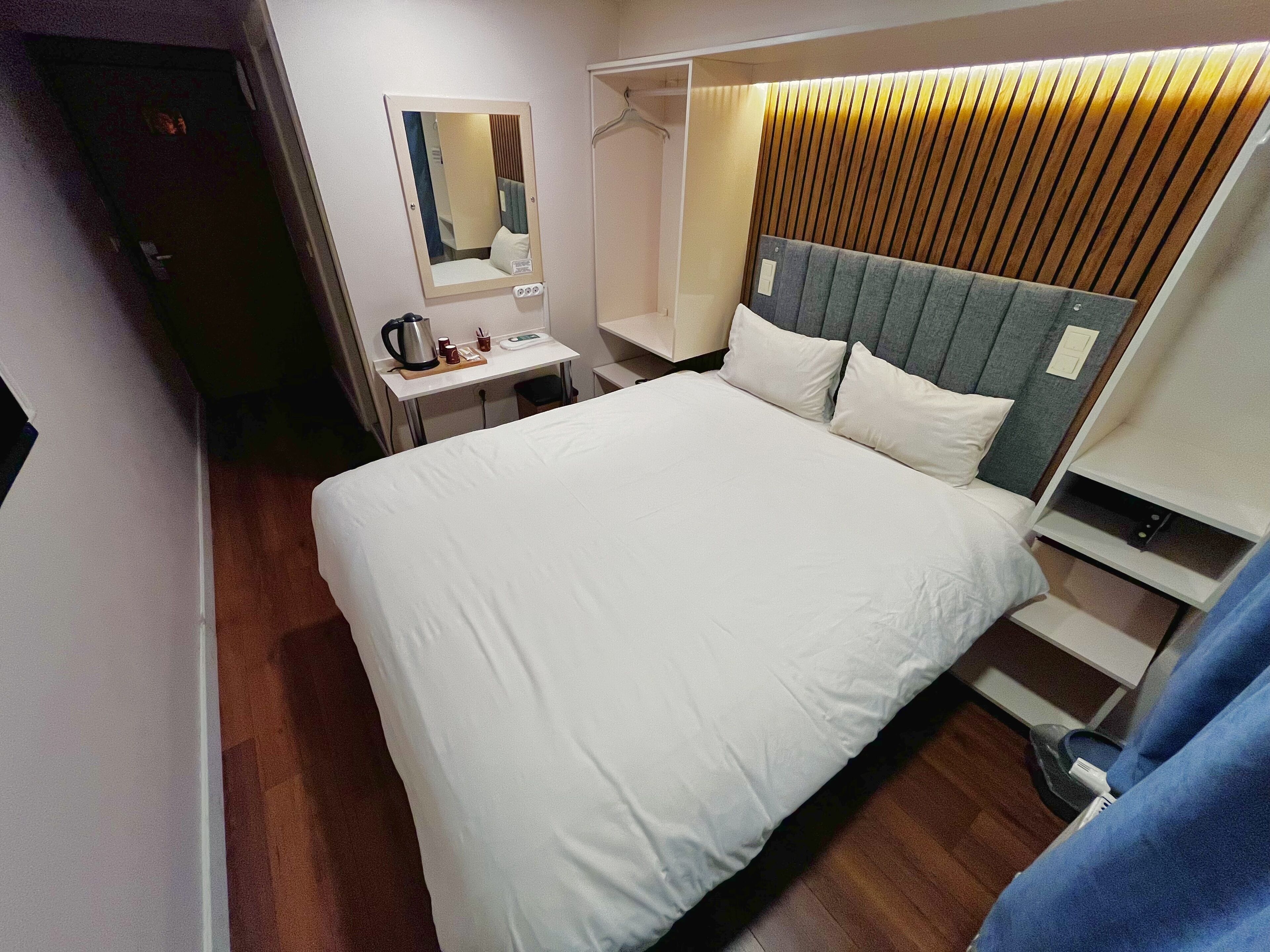 A hotel room with a bed, bedside table, and a mirror.