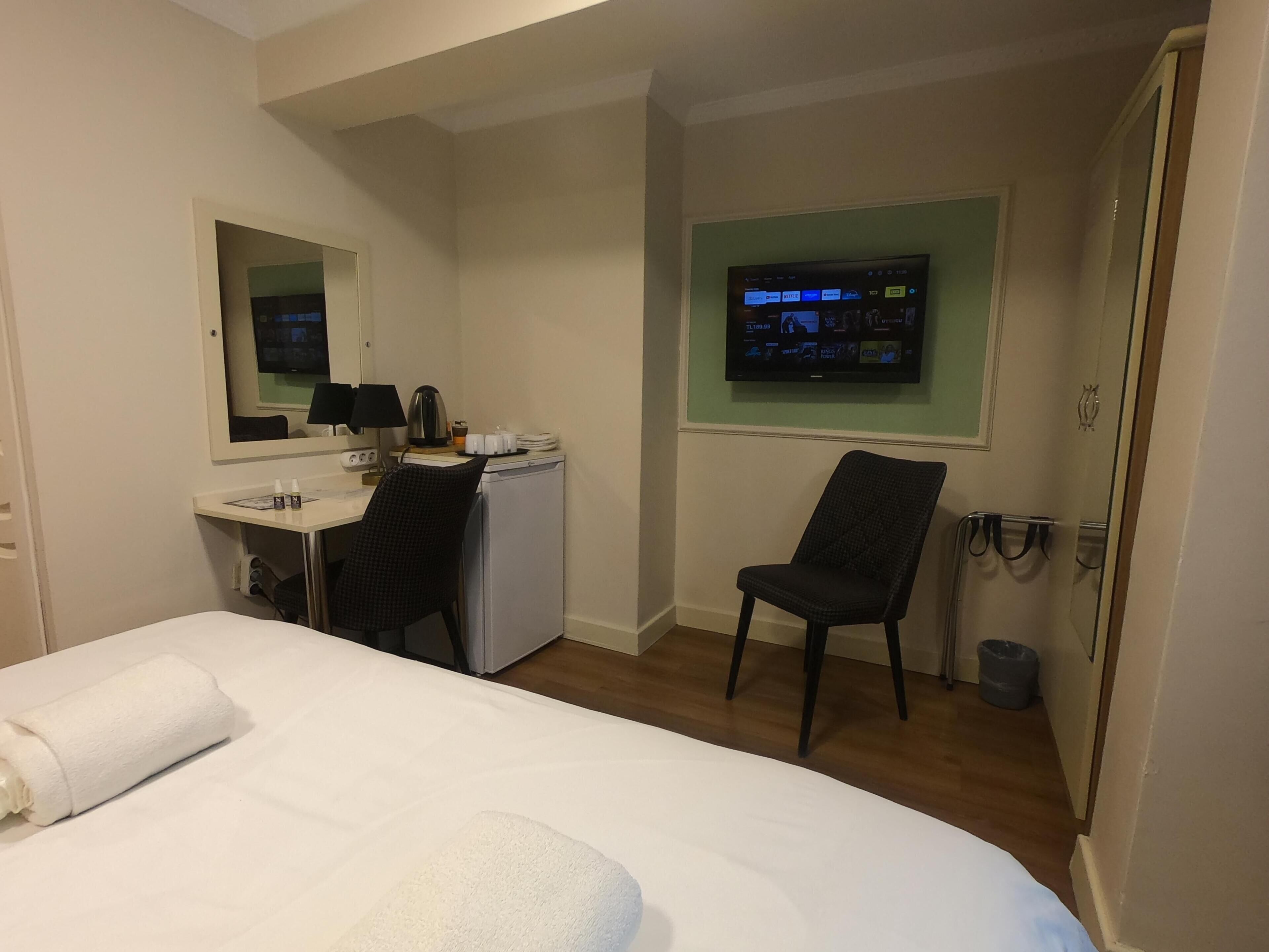 A hotel room with a bed, a desk, a chair, a television, and a mirror.