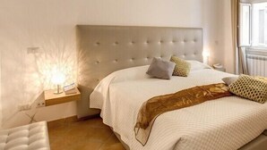 Quarto com cabeceira estofada, mesa de cabeceira com abajur e cama com vários travesseiros.